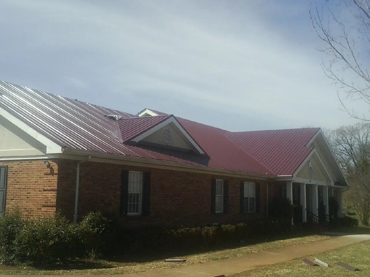 Red metal roof with gabled entries on a long brick building, from a Hail Damage Roof Repair job in Powhattan