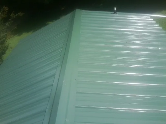 New green metal panels meeting at the ridge of a roof — Flat Roof Repair work by our crew in Powhattan