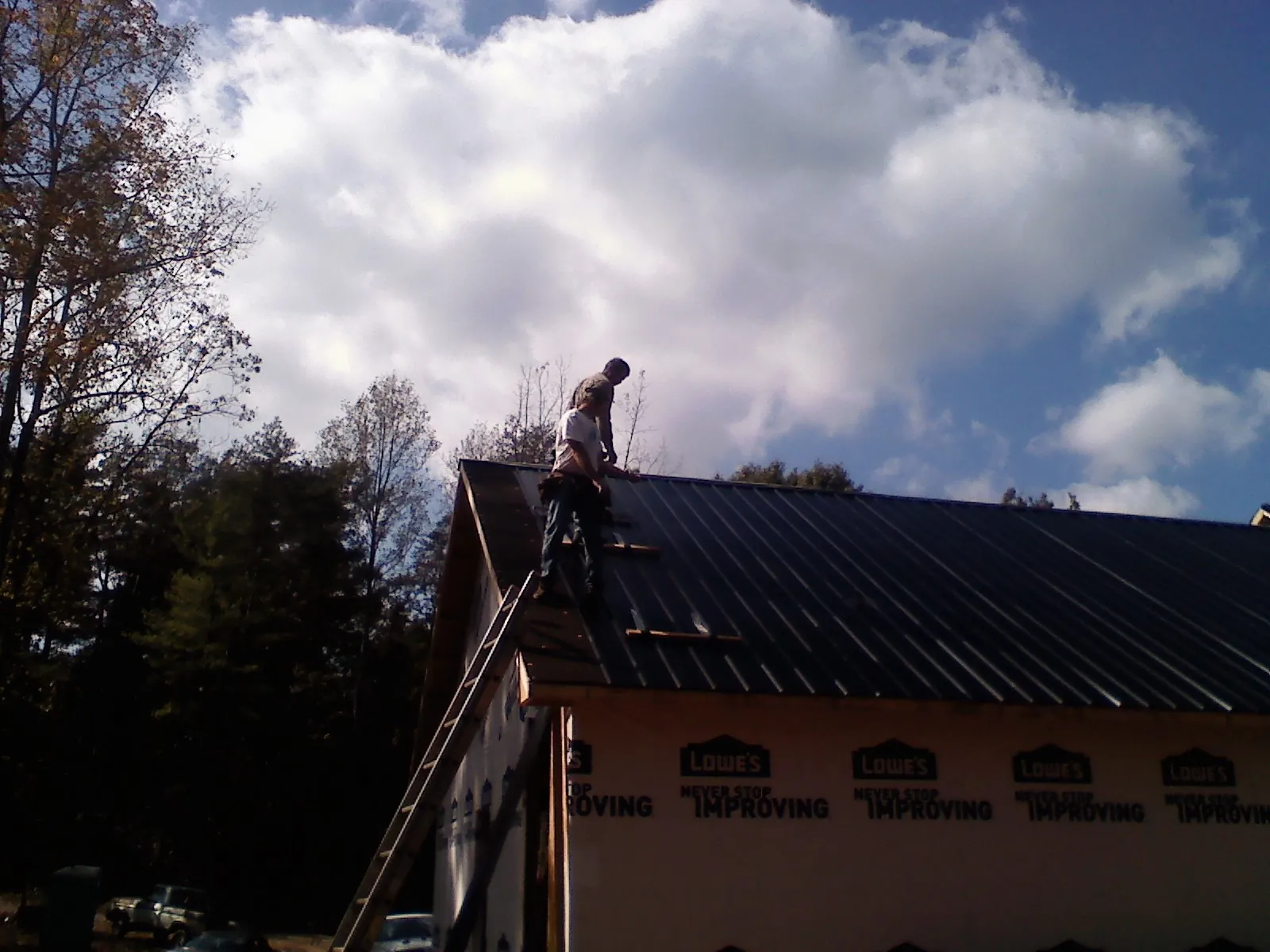 Roofer fastening dark metal panels high against a cloudy sky, from a Roof Inspection job in Powhattan